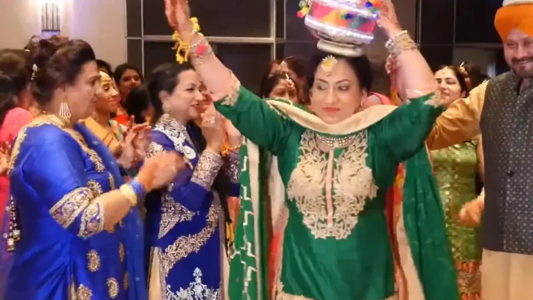 Woman wearing a green traditional outfit and holding a decorative pot on her head during a celebration.